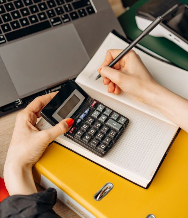 Personne qui calcule le budget de projet OBNL avec une calculatrice, un cahier et une reliure sur un bureau de travail